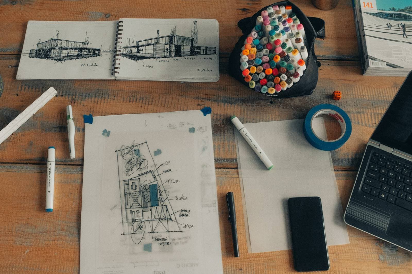 A designer's desk with architectural sketches, markers and a laptop