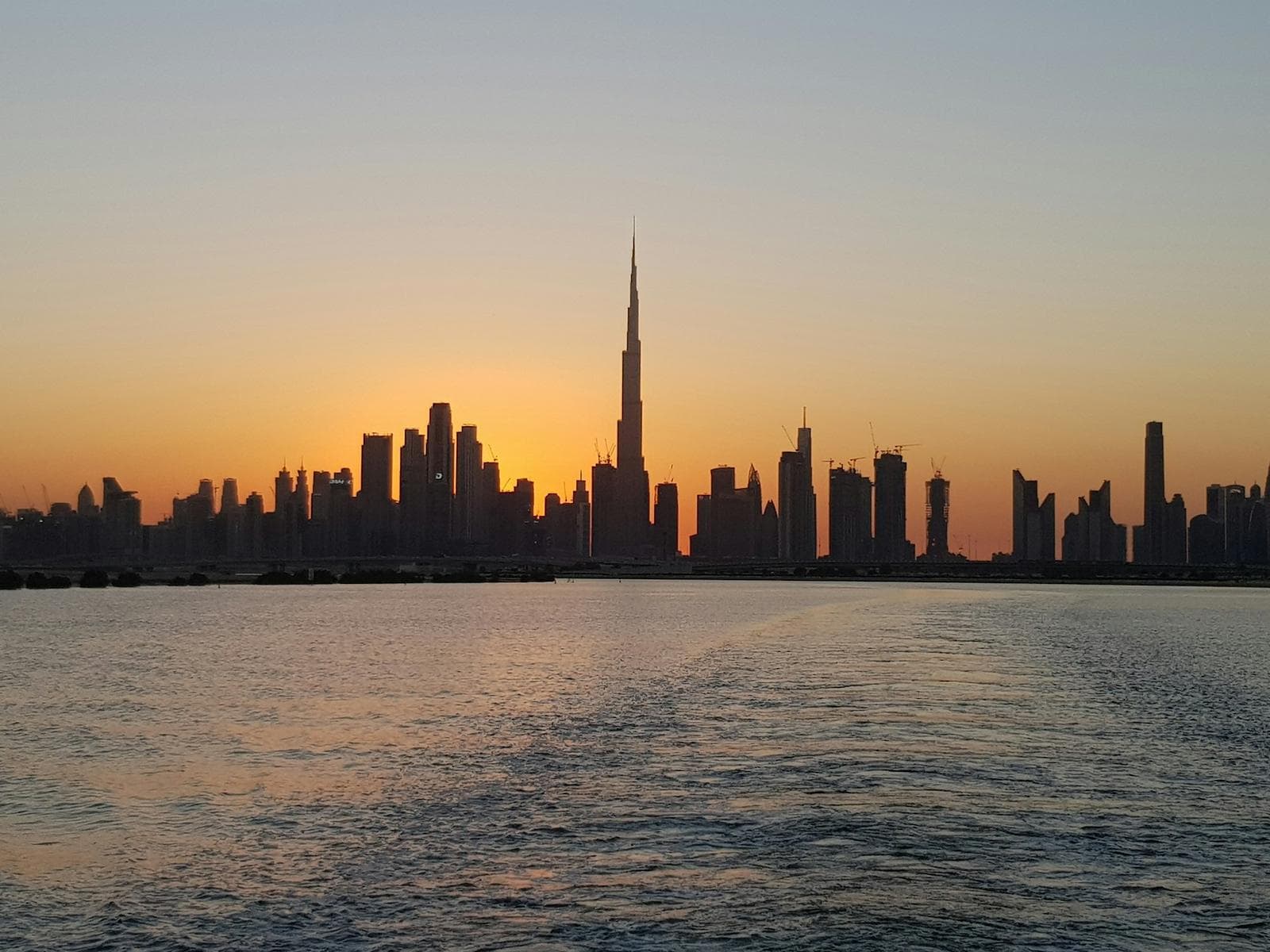 The Dubai skyline in silhouette over calm water at sunset