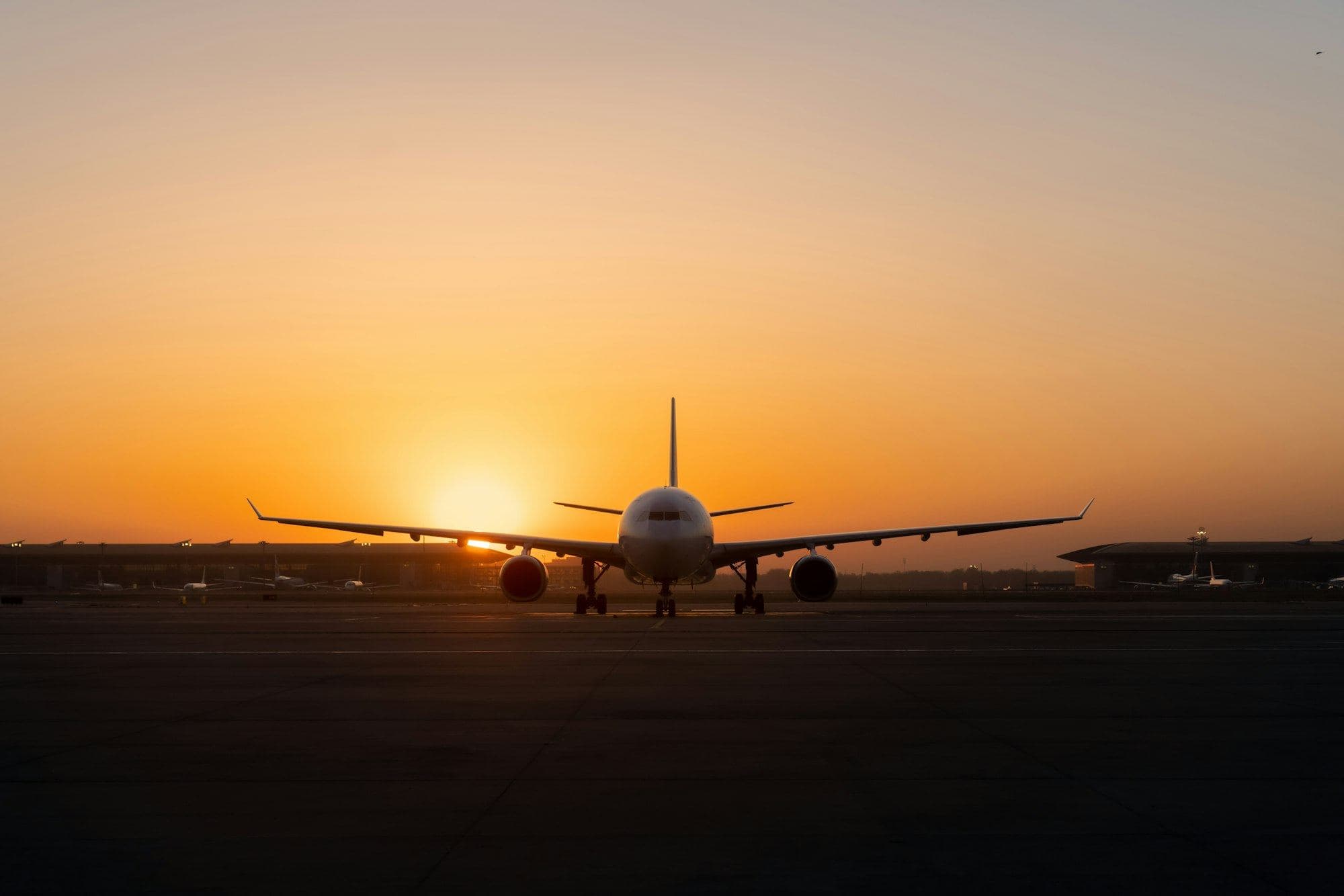 An airliner on the apron, silhouetted against a low orange sun