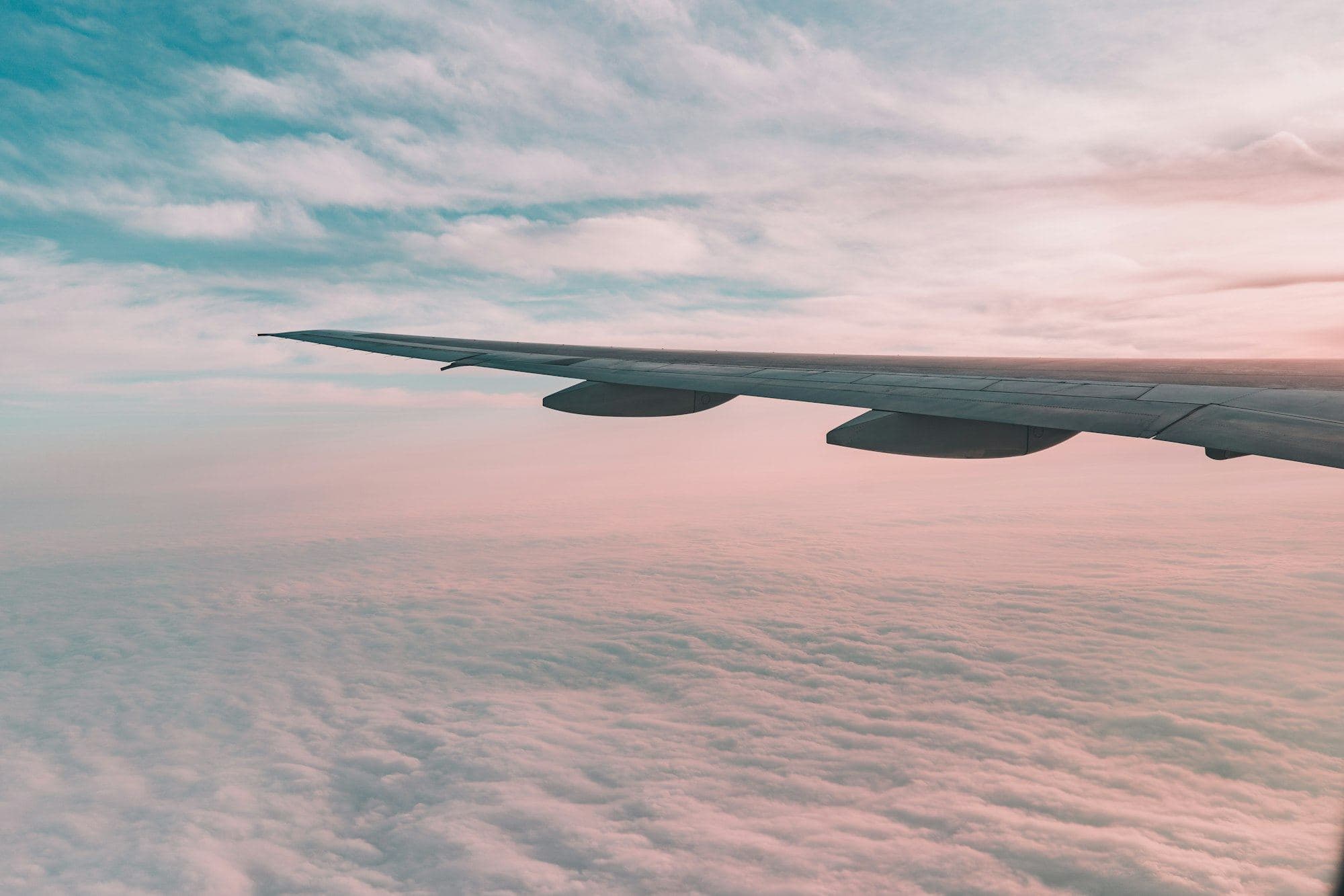 An aircraft wing above pink clouds at dusk